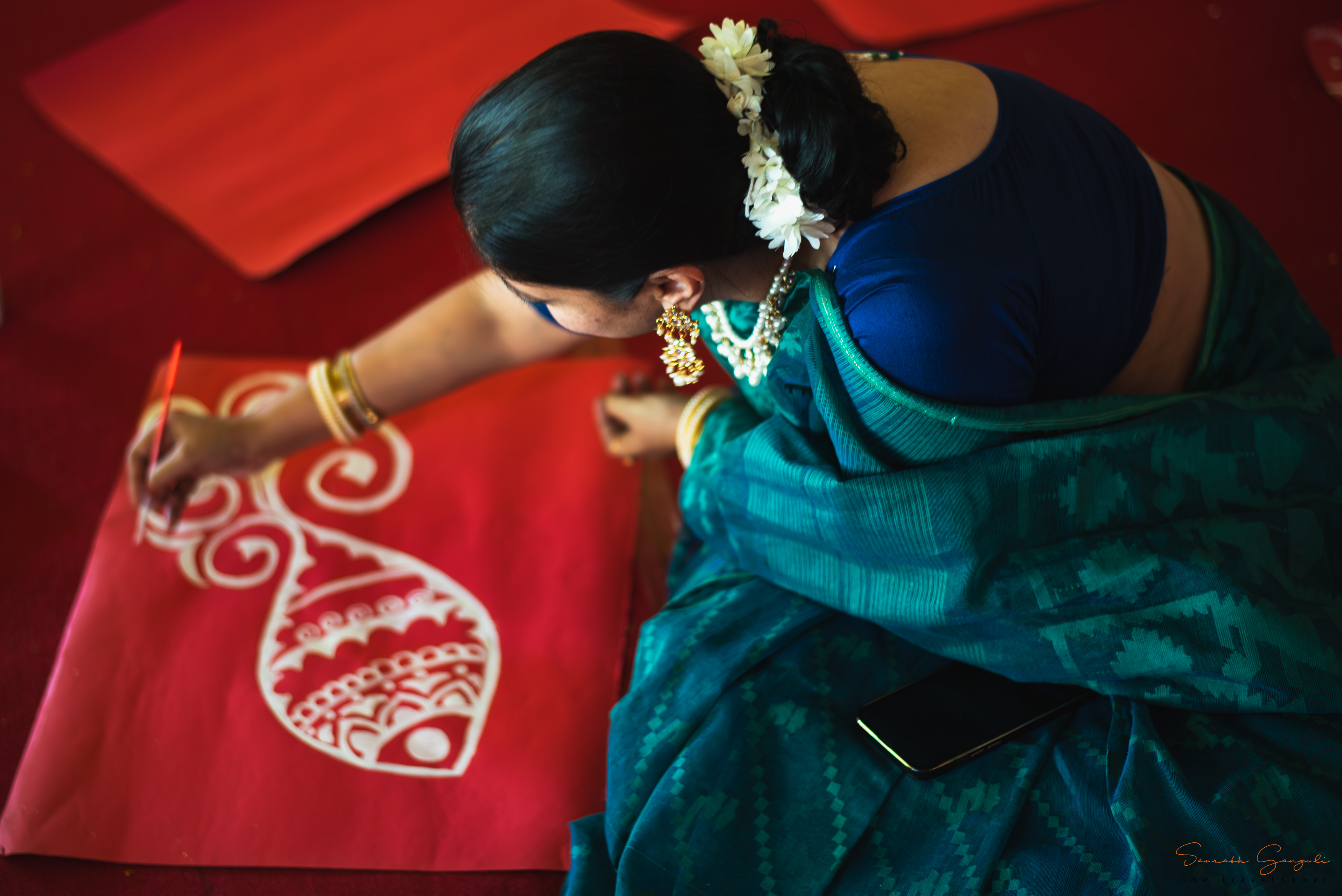 A member of Anandam paints a traditional Bengali alpana in white on red — preparing for the puja.